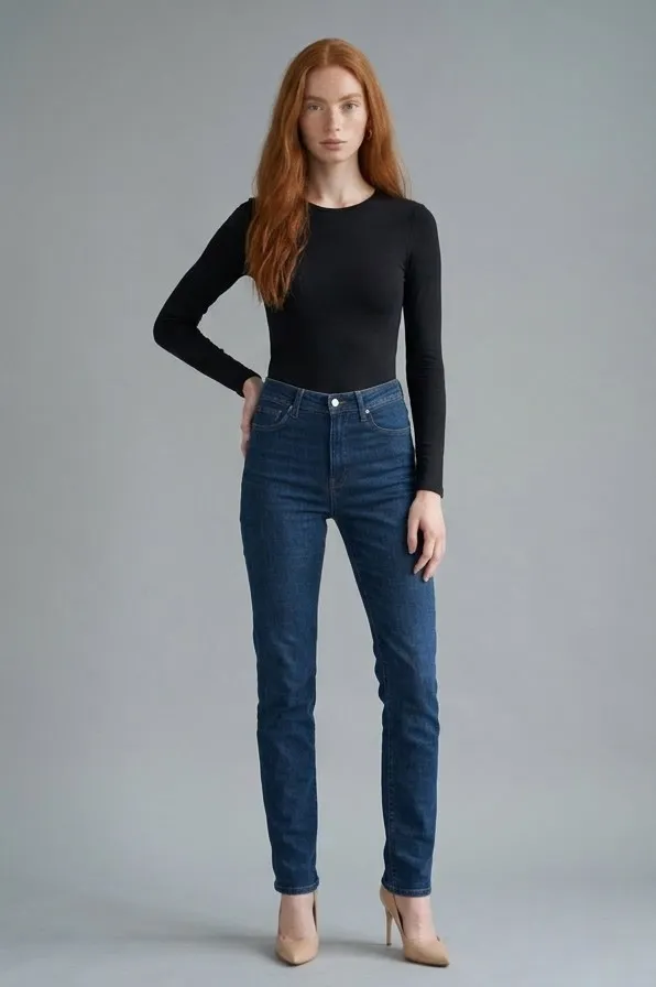 Modelo pelirroja con body negro de manga larga y vaqueros, con una mano en la cadera